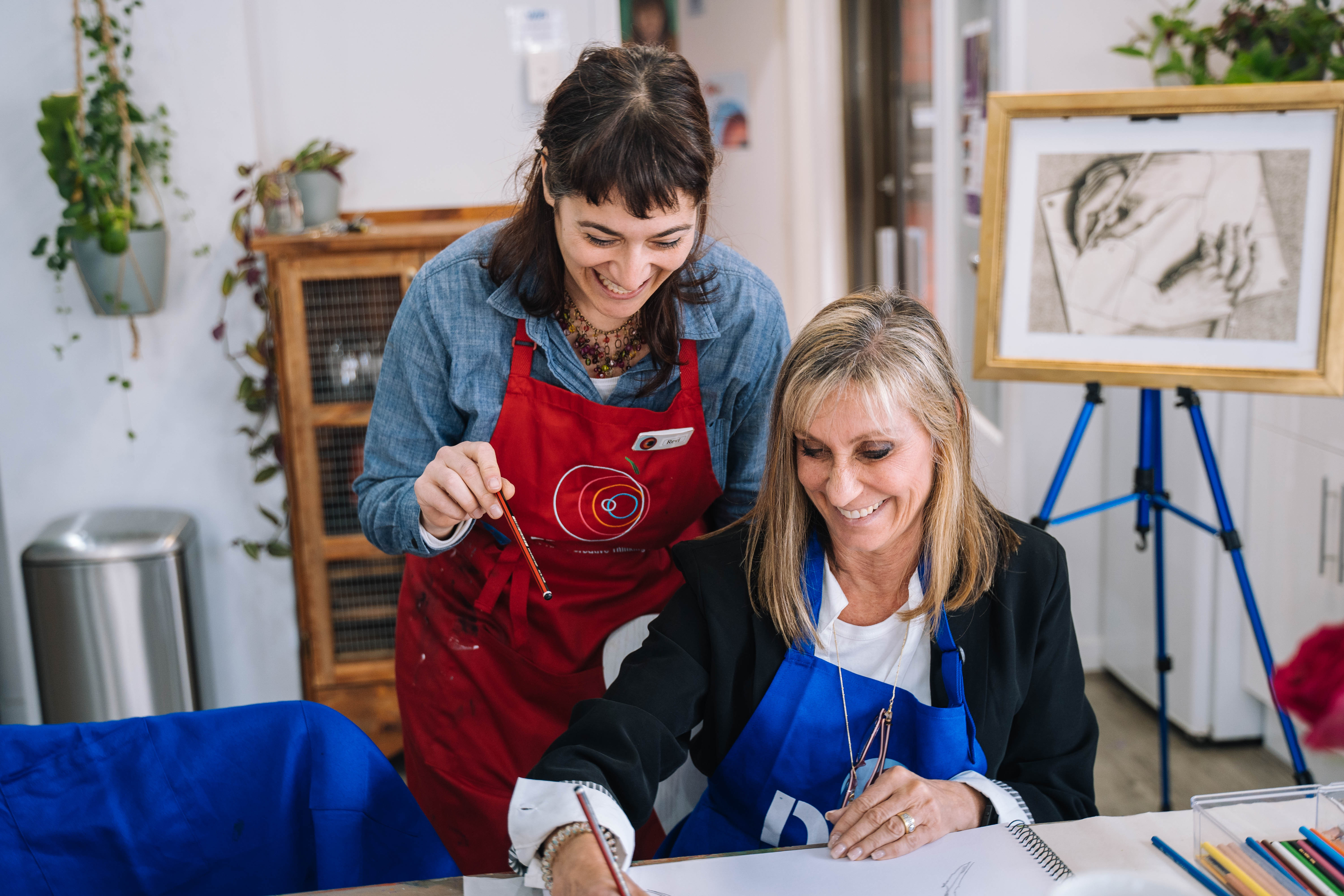 A teacher in an apron assisting a woman at a still life drawing class